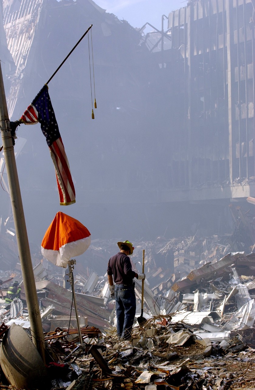 A firefighter stands under the flag of Two World Trade Center and wonders where to begin, 15 September 2001