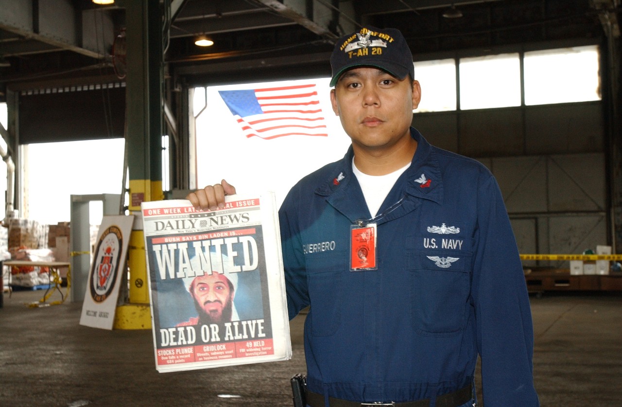 A Petty Officer serving aboard USNS COMFORT (T-AH 20) displays a copy of local newspaper that has a picture of Osama Bin Laden on the cover, 18 September 2001
