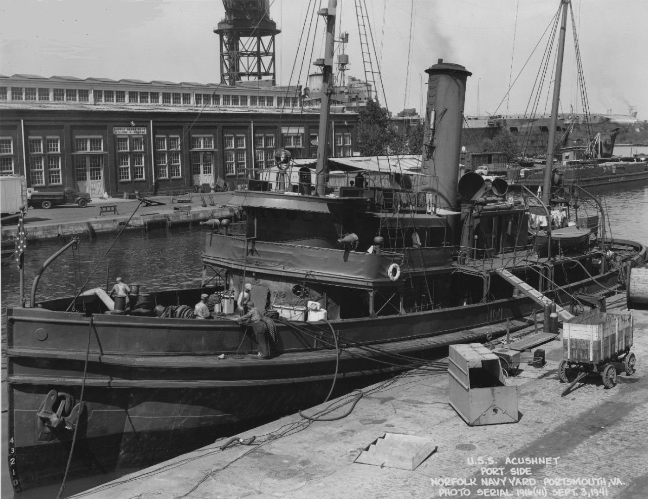 Acushnet moored at the Norfolk Navy Yard, 3 September 1941. The British fleet carrier HMS Illustrious, undergoing repairs after her ordeal off Malta the previous January, can be seen in the background. Also visible are the covered lighter YF-244 ...