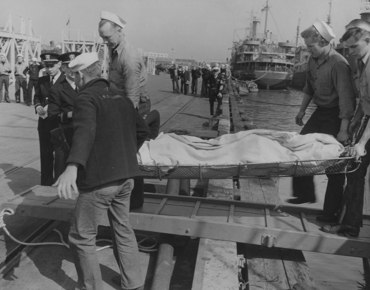 An injured survivor from City of New York is carried on a stretcher by members of Acushnet’s ship’s company (note U.S.S. ACUSHNET stenciled on the back of the coat of the sailor in left foreground), Pier 7, NOB Norfolk, 1 April 1942. Note interes...