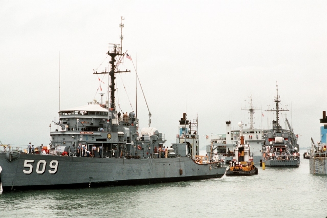 A tug pulls Adroit over Dutch heavy lift ship Super Servant 3 during her deployment to the Persian Gulf War, 19 August 1990. Ocean minesweeper Leader (MSO-490) is to the right. (JO2 Oscar Sosa, Department of Defense Photograph 330-CFD-DN-ST-90-11673, Record Group 330 Records of the Office of the Secretary of Defense, 1921–2008, National Archives and Records Administration).