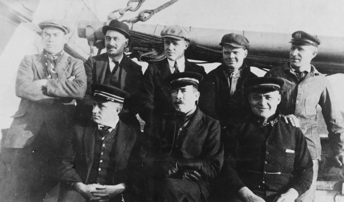 Ship’s officers, wearing civilian clothing, as part of the ship’s disguise as an anti-submarine decoy ship, circa late 1917 or early 1918. Seated in front are (left to right): Lt. John R. Peterson, Jr., Executive Officer and Navigator; Cmdr. Davi...