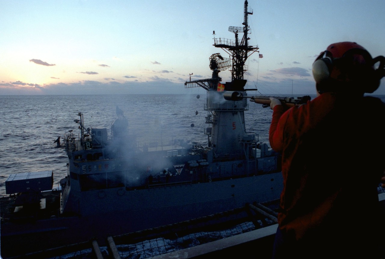 A crewman on board Dwight D. Eisenhower (CVN-69) fires an M14.308 line-throwing rifle toward Capodanno as the latter comes alongside the carrier on 26 February 1988 during preparations for her impending deployment to the Mediterranean. (U.S. Navy Photo by PH2 Gary P. Bonaccorso, Defense Imagery Management Operations Center, Ft. Meade, Md., DN-SC-90-04284)