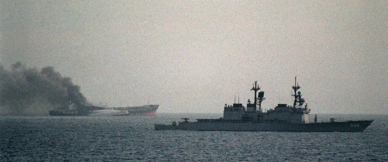 Chandler passes by the burning Greek tanker Ariande as fire tugs attempt to put out the blaze on 15 December 1987. Ariande had been attacked by small gunboats. Just three days prior, Chandler rescued crewmembers of the Cypriot tanker Pivot which had likewise been attacked by gunboats. (U.S. Navy Photograph DN-SC-88-03988, PH2 (Sw) Jeffrey Elliott, National Archives and Records Administration, Still Pictures Division, College Park, Md.)