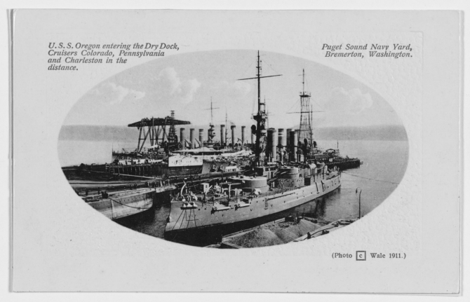 Oregon (Battleship No. 3) enters a drydock at Puget Sound Navy Yard, Bremerton, Wash., circa 1911. The ships in the background are Colorado, Charleston (Cruiser No. 22) -- with her white hull -- and Pennsylvania. Photograph by Wale, printed on a postal card with an embossed area surrounding the image. (Donated by F.M. Deats, 1963, U.S. Navy Photograph NH 3005, Photographic Section, Naval History and Heritage Command)