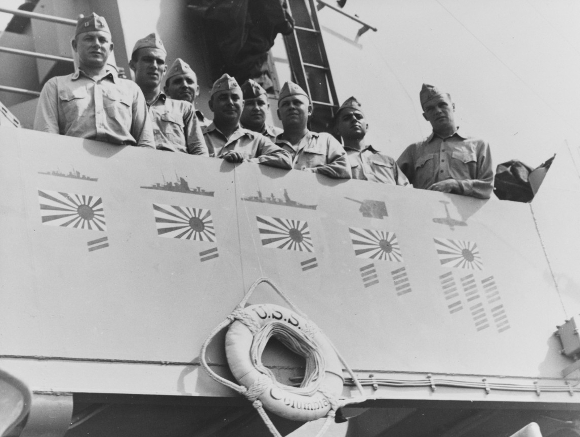 Ship officers (plankowners) pose on Columbia’s bridge wing with her “scorecard” painted just above the life ring, 15 August 1945. (Naval History and Heritage Command Photograph NH 78972)