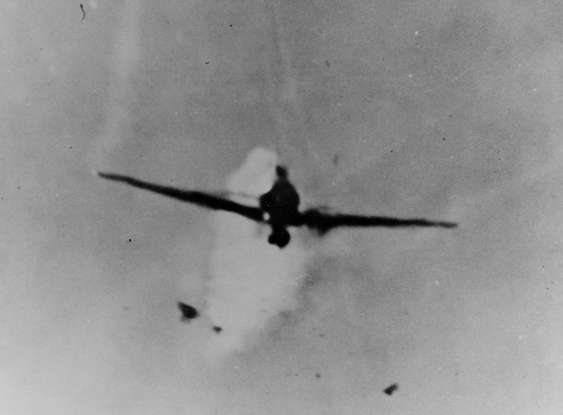 A Japanese Mitsubishi A6M1 Type 0 Zeke diving on Columbia during the Lingayen Gulf operation. The plane is on fire from the ship’s guns. The Zeke was the first of two to crash into the ship this day—showering Columbia's superstructure with gasoli...