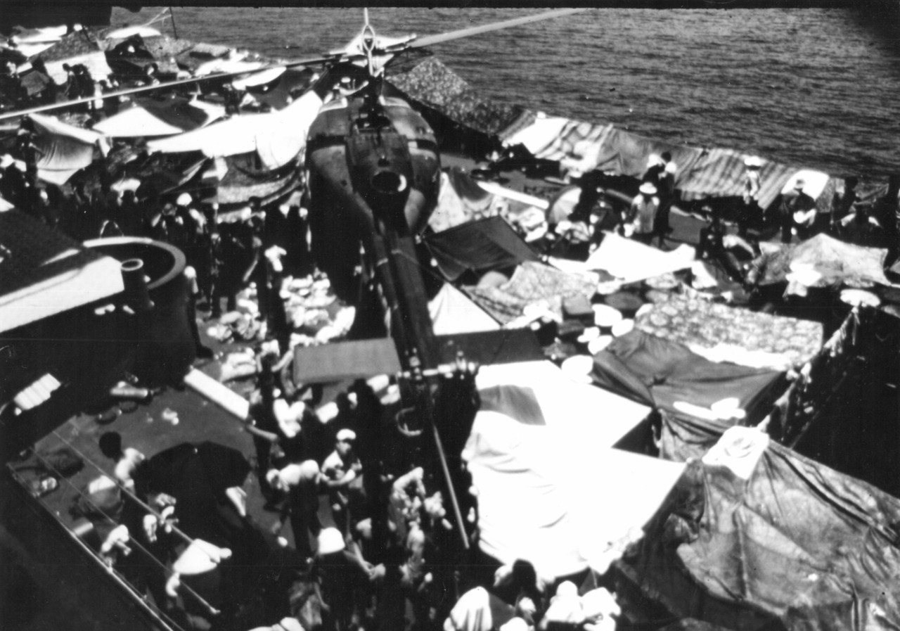 A Huey flies over a ship filled with Vietnamese refugees during Frequent Wind. (NHHC Archives)