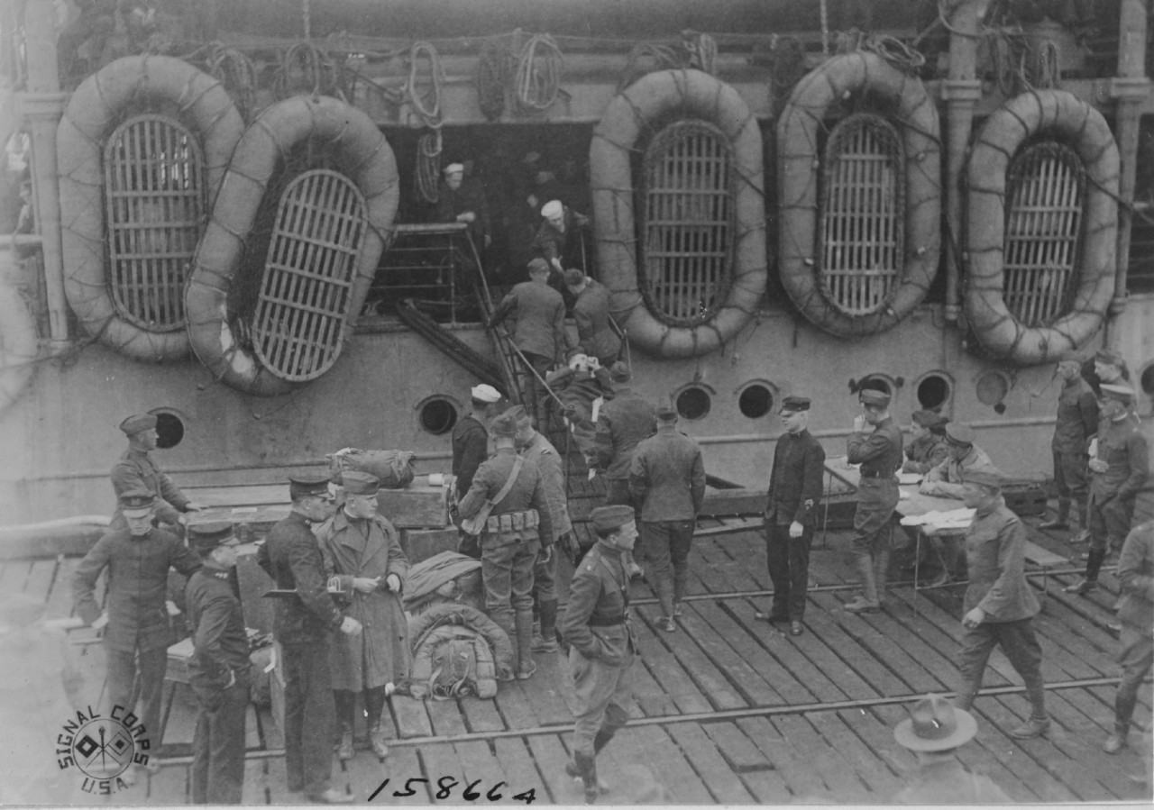 At the head of the gangway, a sailor extends a helping hand to a soldier as they carry a homeward-bound patient as DeKalb embarks passengers for the return voyage to the U.S., 10 May 1919, in this image captured by Cpl. A. T. Lubatty. (U.S. Army Signal Corps Photograph 111-SC-158664, National Archives and Records Administration, Still Pictures Division, College Park, Md.)