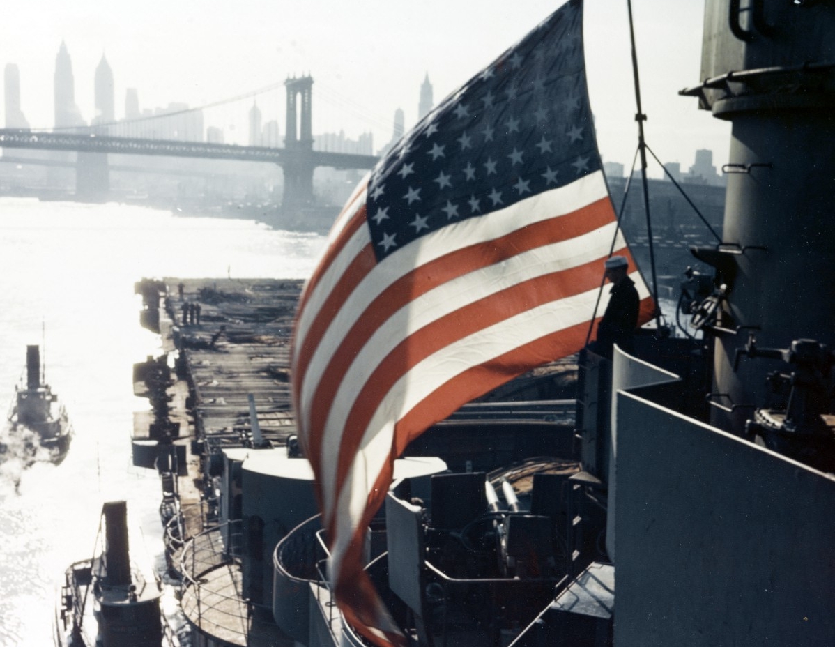 Franklin arrives at the New York Navy Yard for repair of battle damage on 30 April 1945. Photographed looking aft, note her burned-out after flight deck. The Brooklyn Bridge and New York City skyline can also be seen in the background. (U.S. Navy...