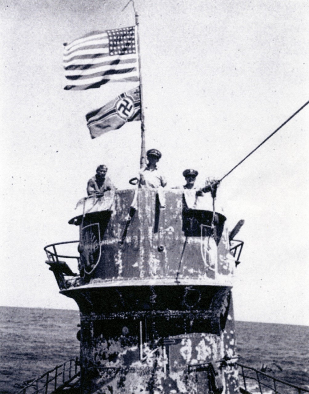 A halftone reproduction of a photograph taken shortly after the boarders seized U-505, 4 June 1944. (Left–right) Lt. (j.g.) David, Capt. Gallery, and Cmdr. Trosino man the conning tower, as the Stars and Stripes flaps above the German naval ensign. The submarine’s hull shows the wear of her long sojourn at sea. (Page 28, Guadalcanal (CVE-60) Memory Log, Ships History, Naval History and Heritage Command Photograph NH 105857)