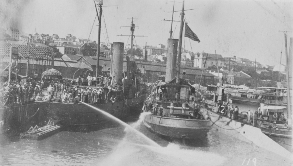 K-2, at right, with other U.S. ships in port, circa 1917-1918. The ship at left appears to be Artemis (S. P. 593), renamed Arcturus in February 1918). That in the center is a tug. They appear to be testing fire hoses. The location is unknown, but...