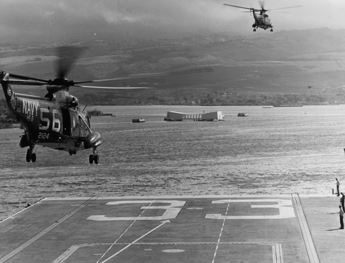 Flight deck sailors watch as a pair of SH-3A Sea Kings (the one on the left is BuNo 152124) of HS-6 lift off from Kearsarge as the carrier enters Pearl Harbor, 27 June 1967. The Arizona (BB-39) Memorial is in the distance. (PH3 B. L. Kleckner, Naval History and Heritage Command Photograph 1124878)