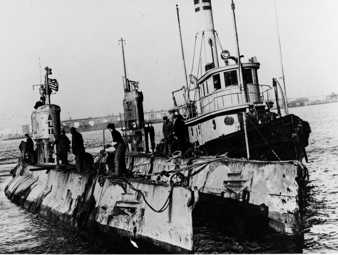 L-11 (Submarine No. 51), at left, still carrying her AL-11 designation, and L-2 (Submarine No. 41) docking at the Philadelphia Navy Yard, assisted by a district tug, circa February 1919. (Naval History and Heritage Command Photograph NH 51176) 