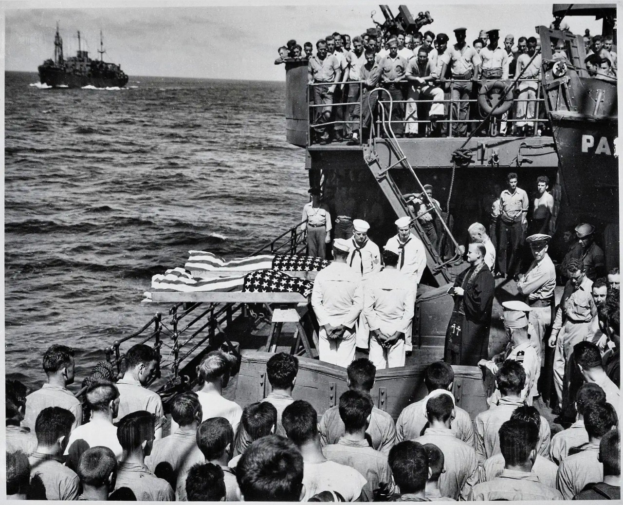 Black and white images showing two flag-draped coffins about to be consigned to the deep with a large crowd of sailors looking on.