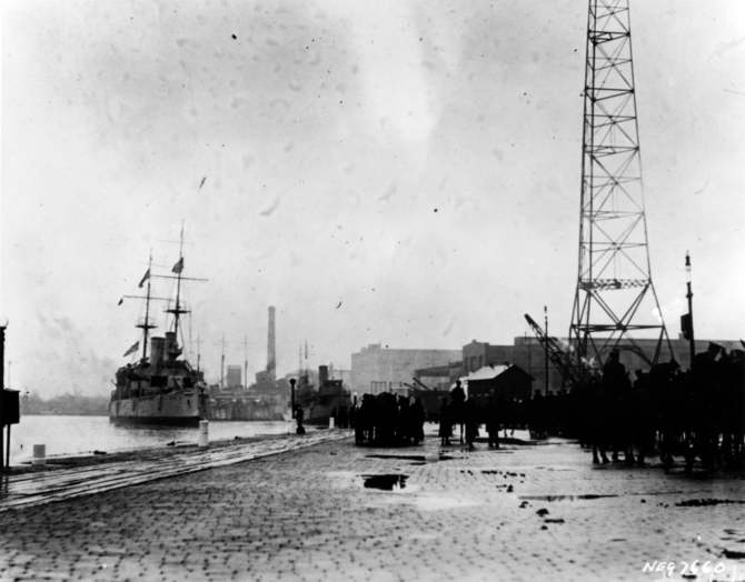 Olympia arrives at the Washington Navy Yard carrying her sacred charge on the otherwise dreary day, 9 November 1921. Destroyers Barney (DD-149) and Blakeley (DD-150) are just visible immediately beyond Olympia’s bow. (Courtesy of Edward Page, 1979, U.S. Navy Photograph NH 89731, Photographic Section, Naval History and Heritage Command)