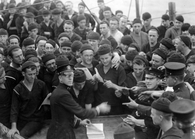 Chaplain distributing the Pennsylvania ship's newspaper to sailors and marines of her crew, circa 1918. Almost all the sailors present are wearing knitted watch caps. (Naval History and Heritage Command Photograph NH 3027)