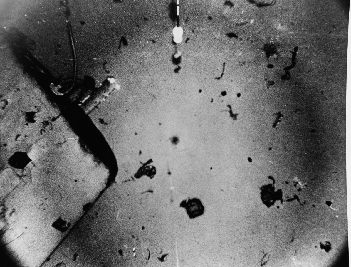 A view of Scorpion’s sail, probably taken when Mizar locates the sunken submarine in October 1968, on the Atlantic Ocean floor 10,000 feet deep, some 400 miles southwest of the Azores. This image shows the starboard side of the sail, with its after end at top left, and the starboard access door in lower left. Debris litters the ocean bottom nearby. The device in top center is part of the equipment used in locating and photographing the wreckage. The original photograph bears the date 30 January 1969. (Naval History and Heritage Command Photograph NH 1136656)