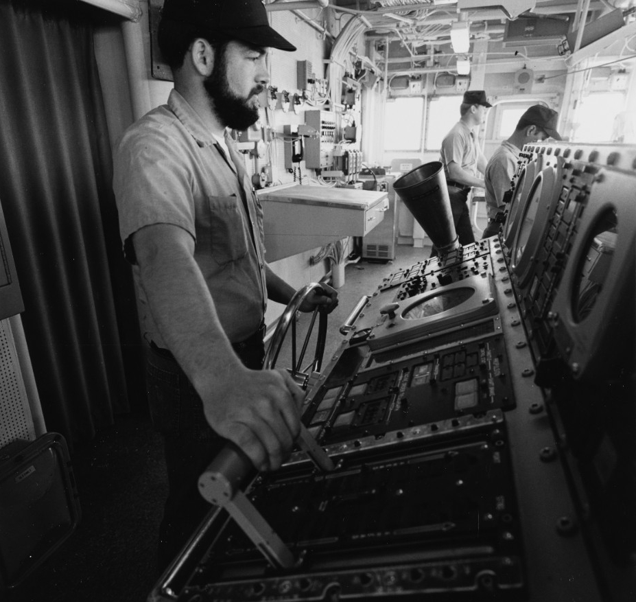 A sailor mans Spruance’s ship control console in the pilothouse during her sea trials in the Gulf of Mexico, May 1975. Other crewmen stand watch as the bridge watch team puts the destroyer through her paces. (Naval History and Heritage Command Ph...