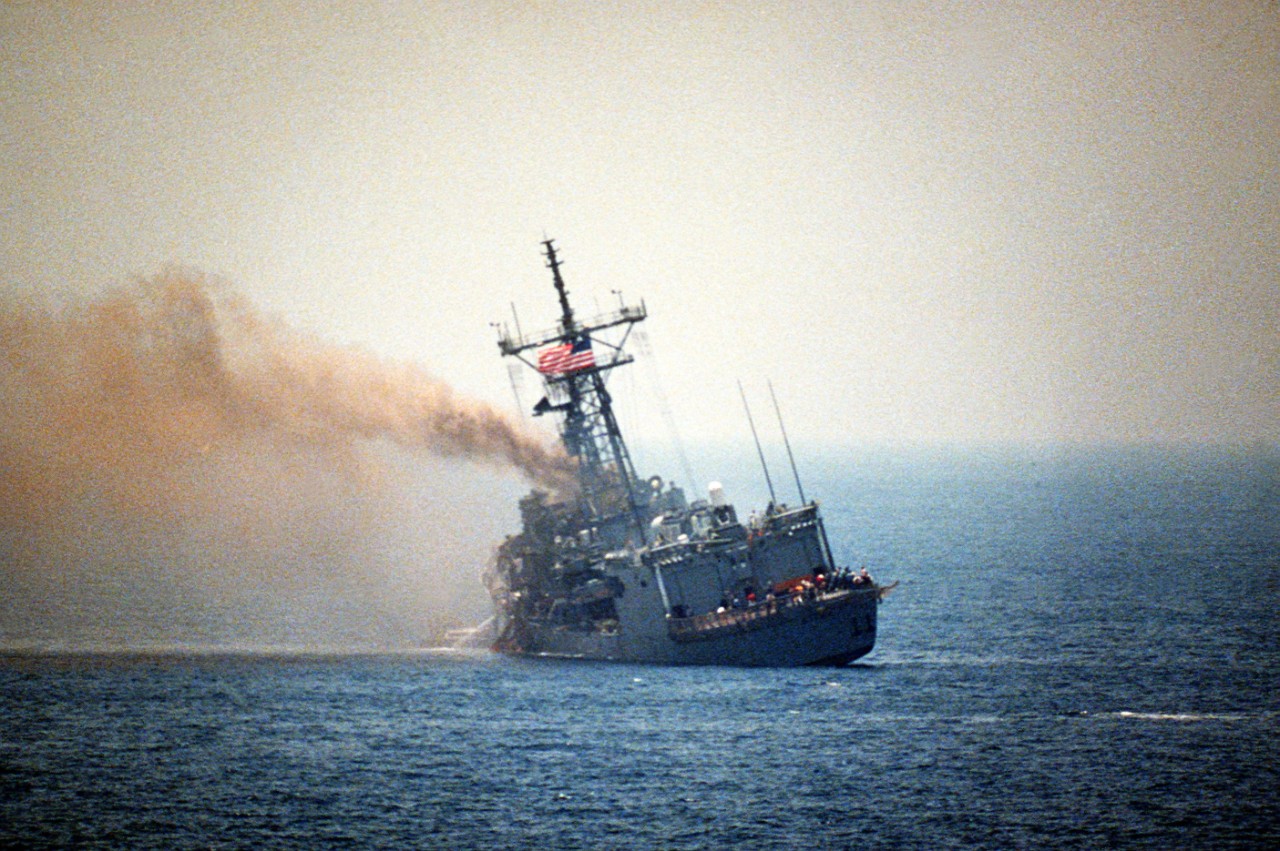 Stark smolders and lists to port the day after two AM.39 Exocet air-to-ground missiles slam into her in the Arabian Gulf, 18 May 1987. The ship proudly flies her colors, crewmen lean precariously to starboard on her flight deck while inspecting the damage, and water pours from her port side as fire-fighters dewater the frigate. (Department of Defense Photograph DN-SC-87-06412, Still Pictures Branch, National Archives and Records Administration II, College Park, Md., Photograph 6417925)