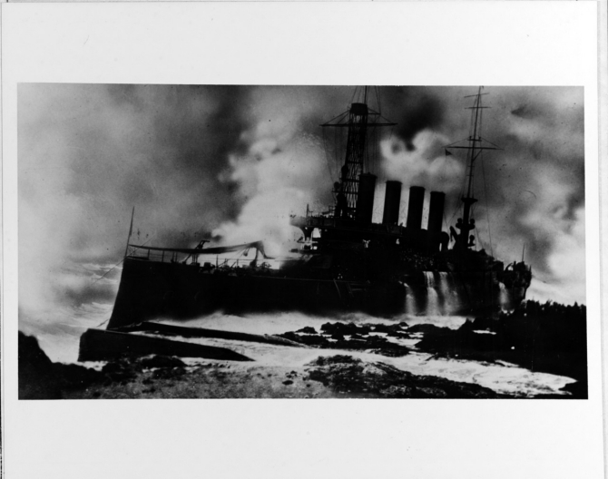 Men on the bridge and superstructure amidships cling to the ship as waves break over Memphis and steam rises furiously, in this picture taken during the late afternoon. This photograph appears to have been retouched. (U.S. Navy Photograph NH 65672, Photographic Section, Naval History and Heritage Command)