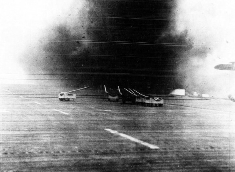The Zeke suicide plane crashes scant yards from the ship, the explosion showering debris across the flight deck and hangar enclosure, 25 October 1944. (White Plains (CVE-66), Ships History, Naval History and Heritage Command)