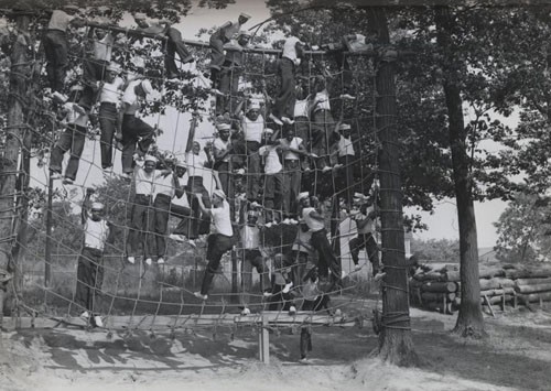 "A cargo net, such as is used to hoist supplies aboard ship, is used to teach the recruit to climb ship ladders. Invaluable physical exercise is also gained on this barrier. 9 September 1942."