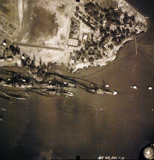 80-G-387572:  Pearl Harbor Attack, 7 December 1941.  Aerial view of "Battleship Row" moorings on the southern side of Ford Island, 10 December 1941, showing damage from the Japanese raid three days earlier.  Diagonally, from left center to lower right are: USS Maryland (BB-46), lightly damaged, with the capsized USS Oklahoma (BB-37) outboard. A barge is alongside Oklahoma, supporting rescue efforts. USS Tennessee (BB-43), lightly damaged, with the sunken USS West Virginia (BB-48) outboard. USS Arizona (BB-39), sunk, with her hull shattered by the explosion of the magazines below the two forward turrets. Note dark oil streaks on the harbor surface, originating from the sunken battleships.  Photographed by VJ-1 at an altitude of 3,000 feet and released November 9, 1950. U.S. Navy photograph, now in the collections of the National Archive.     (9/22/2015).