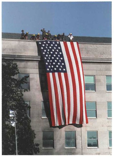 Firefighters and military personnel unfurl the flag from the Pentagon roof during President Bush's visit on 12 September 2001.