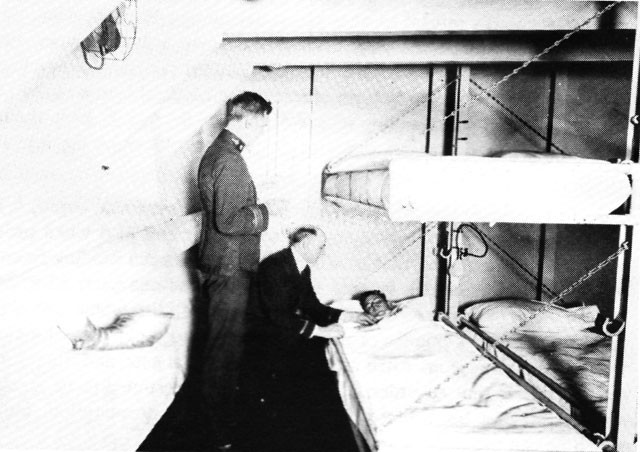 Image of Medical Officer and Chaplain with a patient in sickbay of USS Relief, circa 1920. 