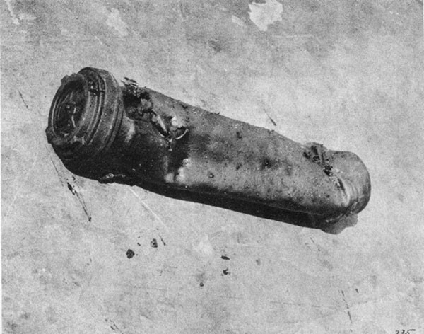 KILLEN (DD597). A typical burned-out powder cartridge can recovered from A-408-M. It has been crushed by blast, punctured by fragments, and powder inside burned out. Some unburned powder grains cling to the exterior surface.