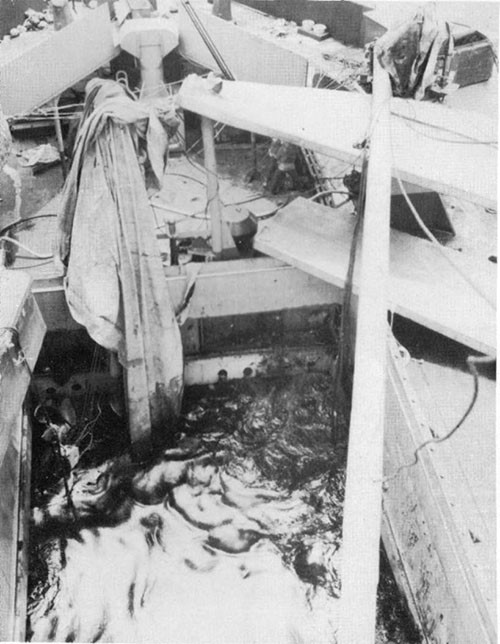 Photo 22: Damage to shelter deck, looking aft from forward of No. 5 hatch. Note displaced 5-ton hatch covers and fallen 10-ton boom.