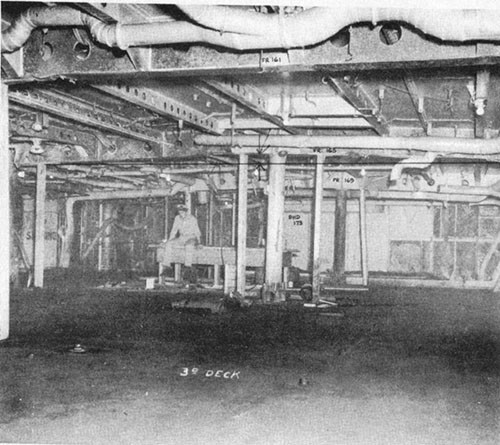 Photo E-9: First hit. View of port after corner of D-303-1L. Note bulge in overhead and temporary angles welded between stanchion and third deck.