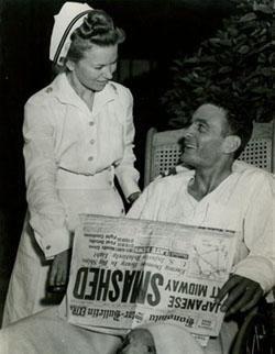 Ensign George H. Gay at Pearl Harbor Naval Hospital, with a nurse and a copy of the 'Honolulu Star-Bulletin' newspaper featuring accounts of the battle. He was the only survivor of the 4 June 1942 Torpedo Squadron Eight (VT-8) TBD torpedo plane attack on the Japanese carrier force. Gay's book 'Sole Survivor' indicates that the date of this photograph is probably 7 June 1942, following an operation to repair his injured left hand and a meeting with Admiral Chester W. Nimitz.