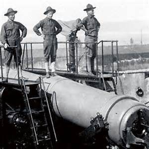 A picture of a three-man crew standing on top of their gun at a coastal fortification.