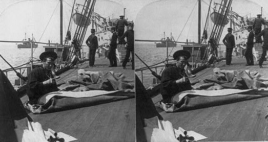 A photo of sailors mending a sail on a ship's deck.