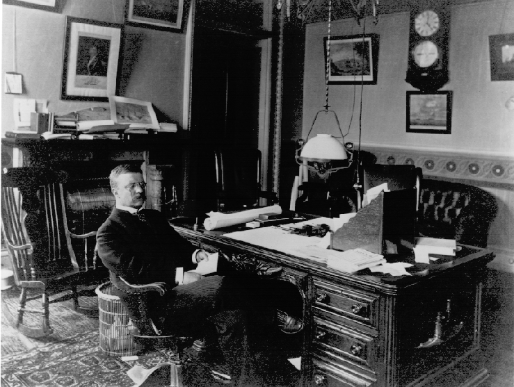 Asst. Secretary of the Navy Theodore Roosevelt, who is sitting at his desk, encouraged the development of war plans against the Kingdom of Spain.