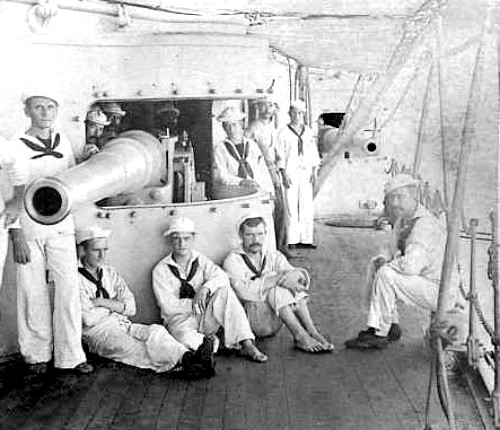 Some men of the USS Olympia lounging by a gun.