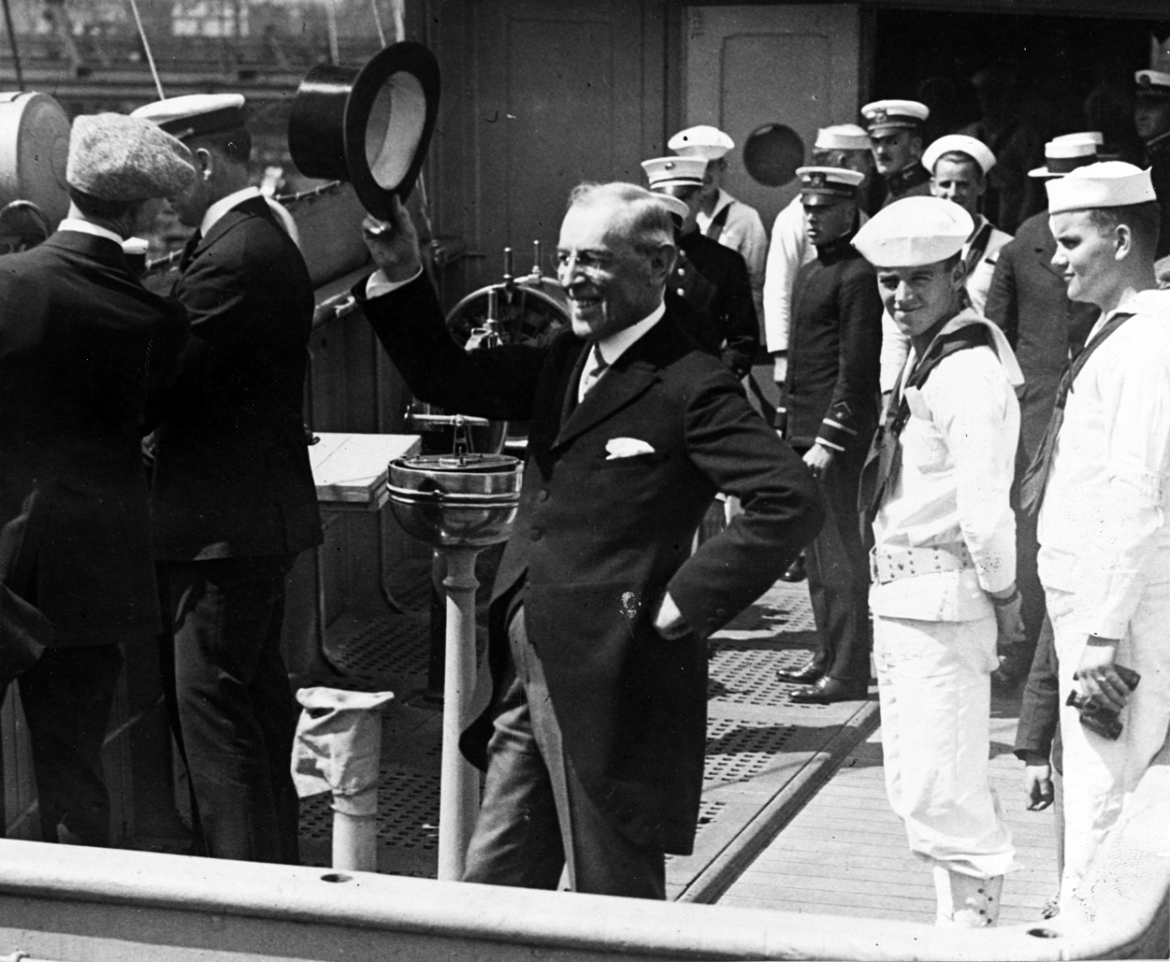 Photograph of Wilson raising his hat as he exits the ship. A row of sailors stands behind.