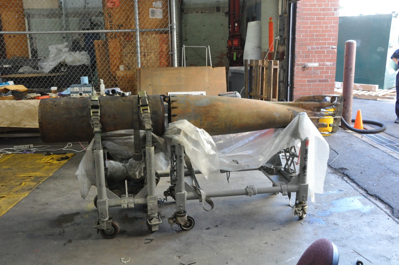 <p>The mid and tail-sections of Howell torpedo No.24 midway through conservation placed end to end on a torpedo cart in the NHHC warehouse.</p>
