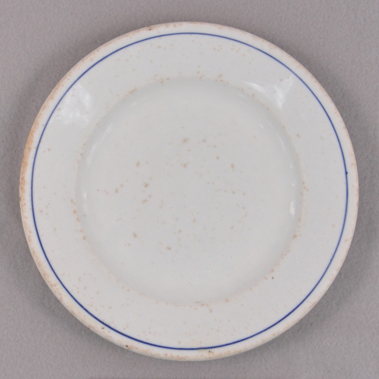 <p>A white glazed stoneware plate recovered from USS San Diego with a blue line border around its edge.</p>