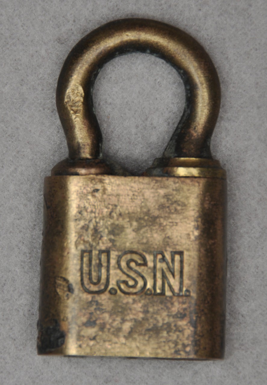 <p>A padlock with a brass case and shackle has the “U.S.N” engraved on the front.</p>
