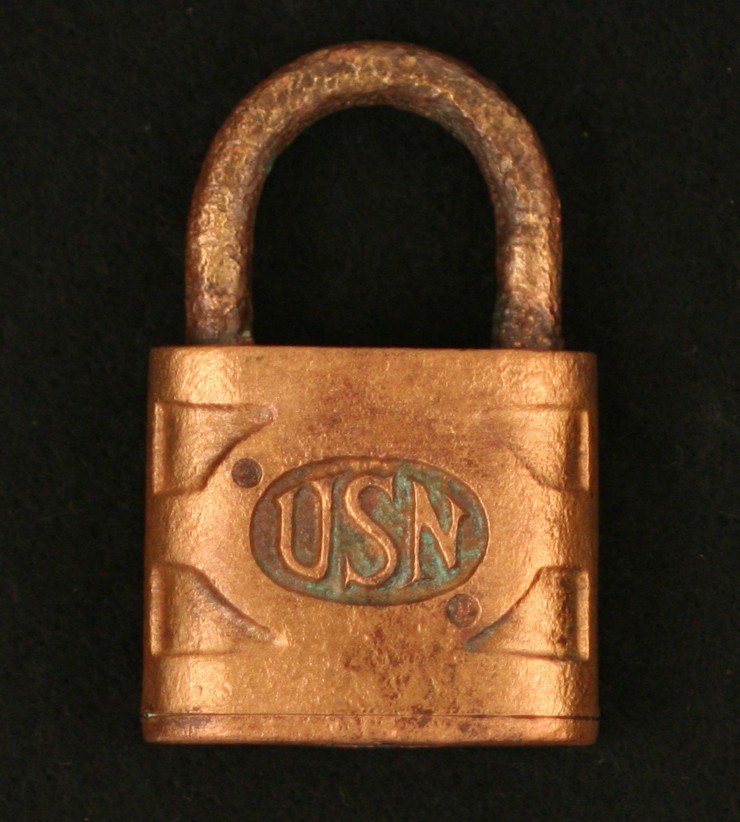 <p>A padlock with a brass case and shackle has the “U.S.N” cast on the front inside a circle.</p>
