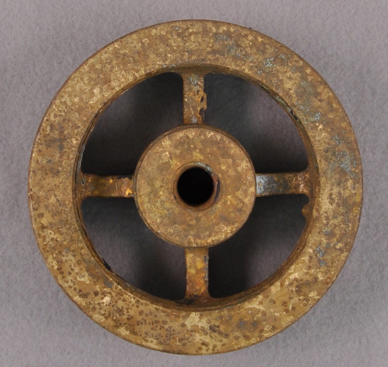 <p>A brass circle with four square rods connected to a smaller circle inside. The smaller circle has a hole in the middle of it.</p>
