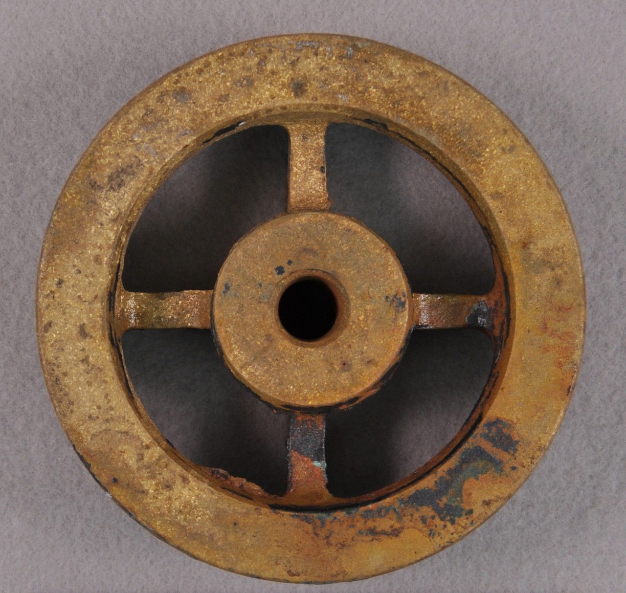 <p>A brass circle with four square rods connected to a smaller circle inside. The smaller circle has a hole in the middle of it.</p>
