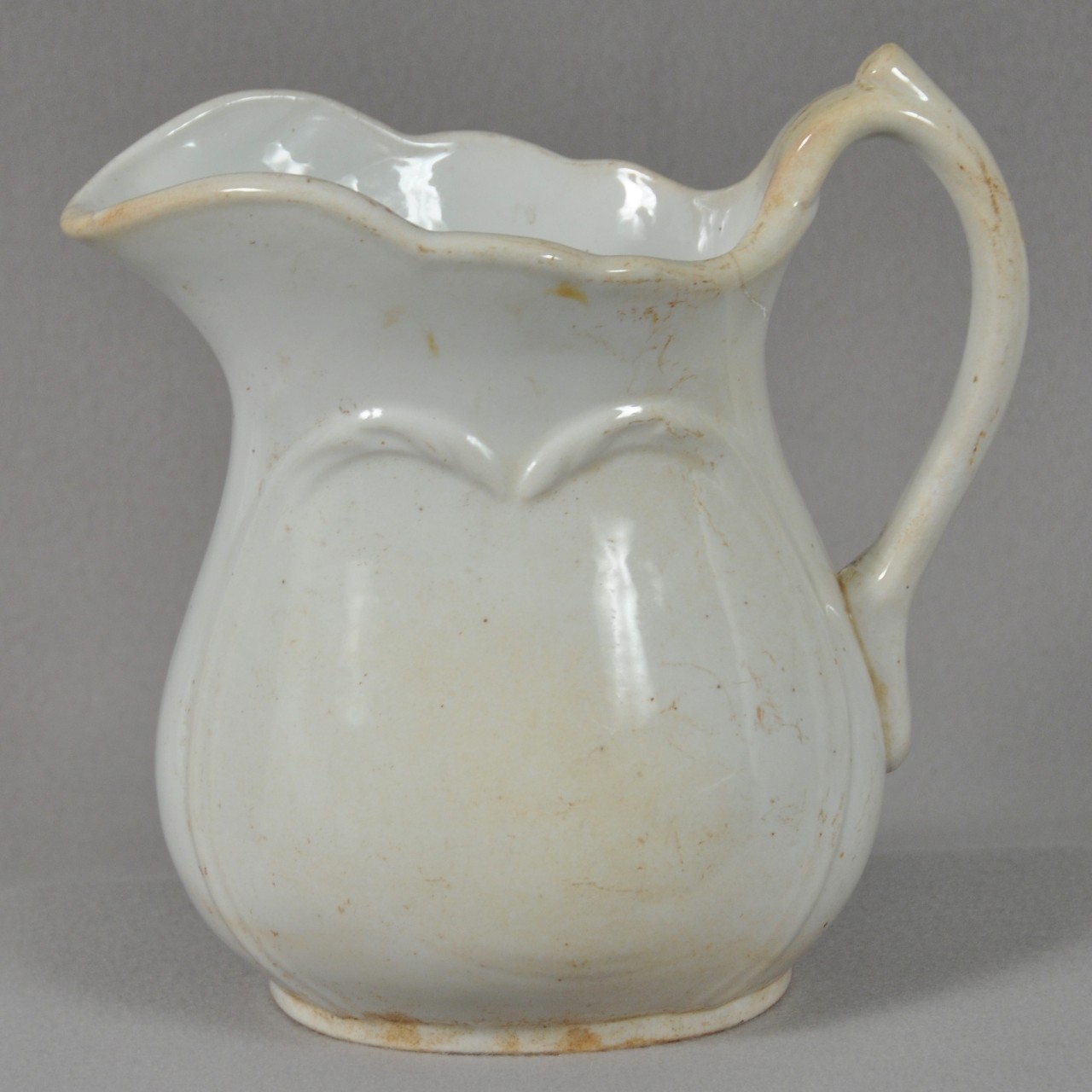 <p>A white glazed stoneware pitcher with decorative molding on both sides from USS San Diego.</p>
