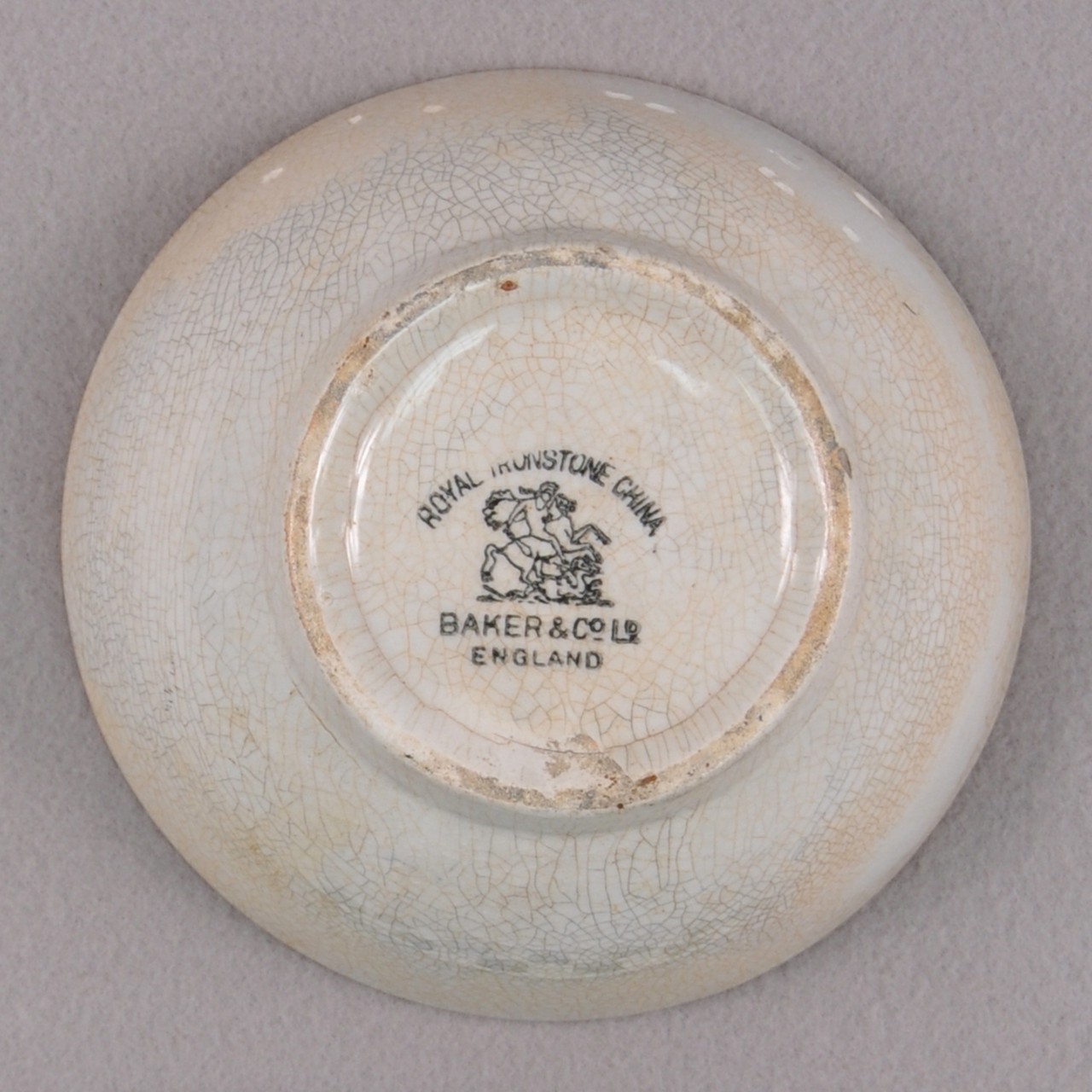 <p>An undecorated white stoneware bowl with cracked glaze from USS San Diego. A maker’s mark of a man riding a horse and the words “Royal Ironstone China” and “Baker &amp; Co Ltd. England” around the mark located at the bowl’s base.</p>