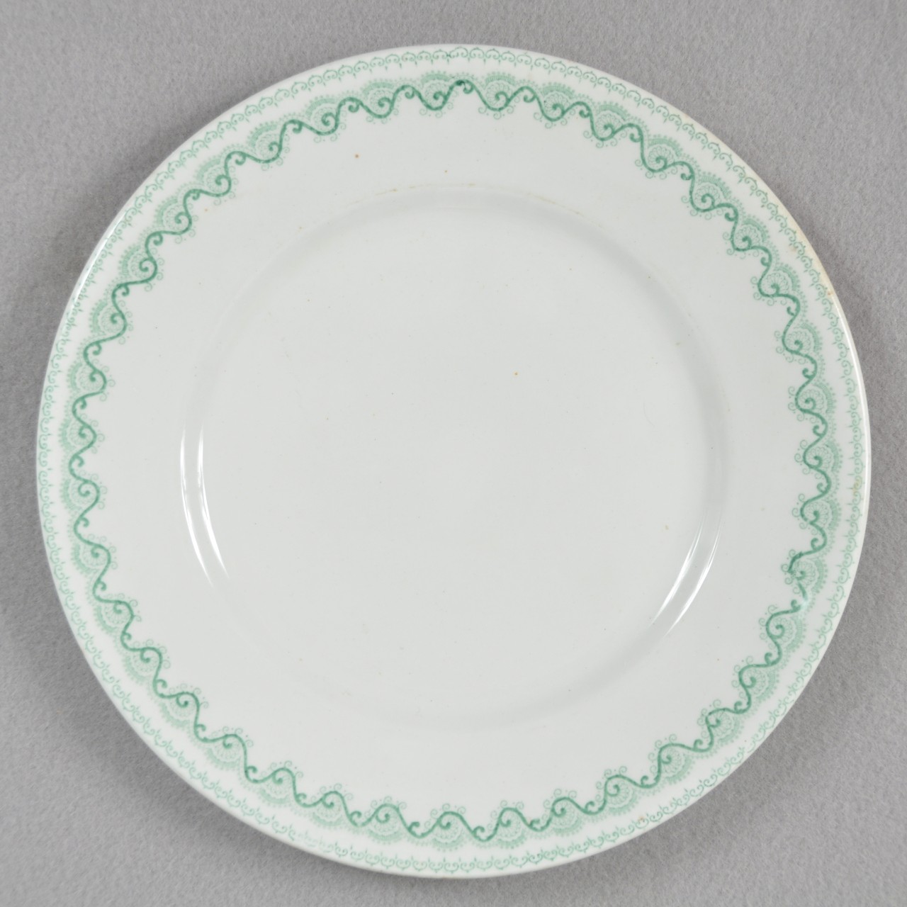 <p>A white glazed stoneware plate recovered from USS San Diego with a continuous green scrolling pattern around the border.</p>