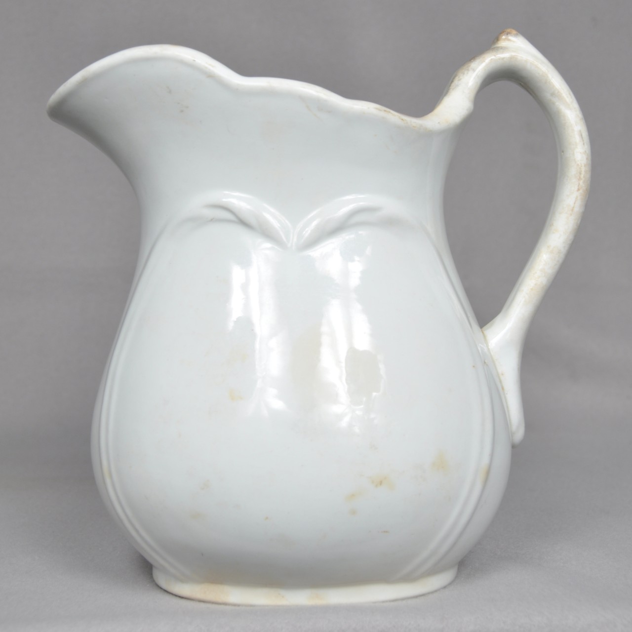 <p>A white ceramic pitcher with decorative molding on both sides.</p>

