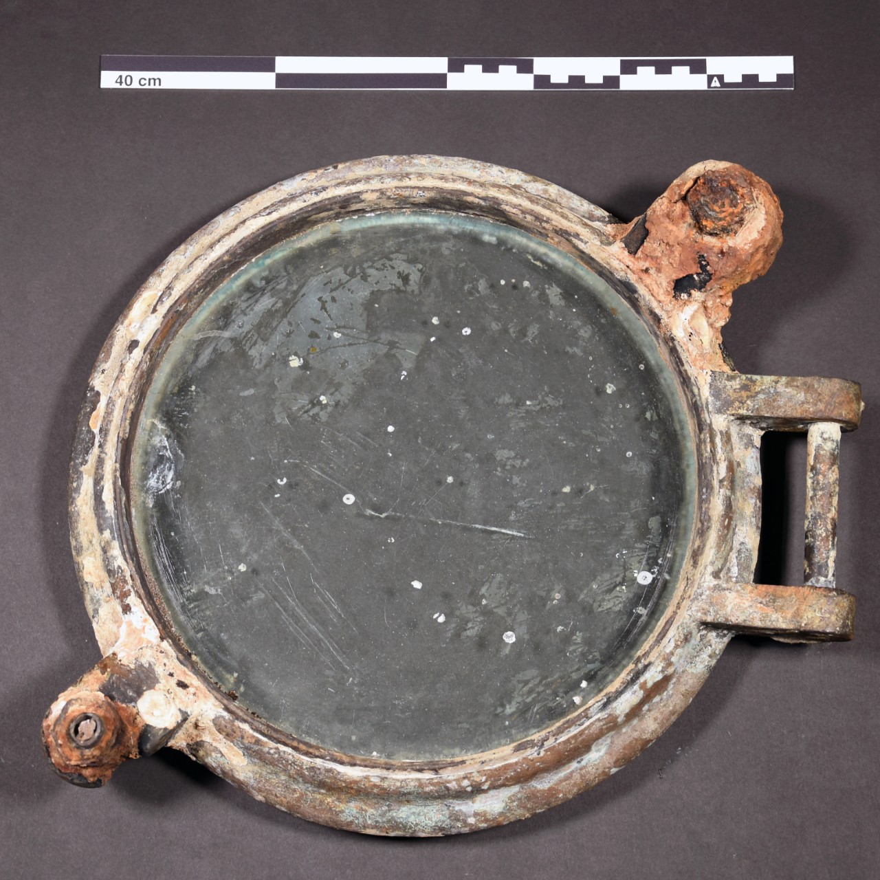 <p>Thick circular brass rim with a circular clear glass inside.&nbsp; Covering both the brass and glass are barnacles, compacted sand, red and green corrosion.</p>
